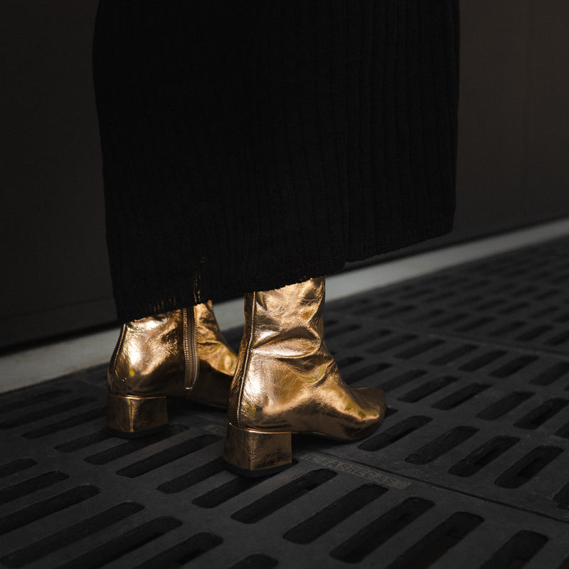 Un par de botines dorados para mujer vistos de ángulo trasero