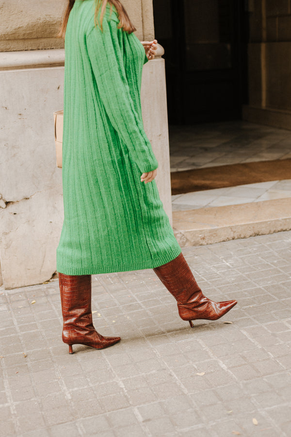 Mujer con vestido verde largo con unas botas altas marrones efecto cocodrilo
